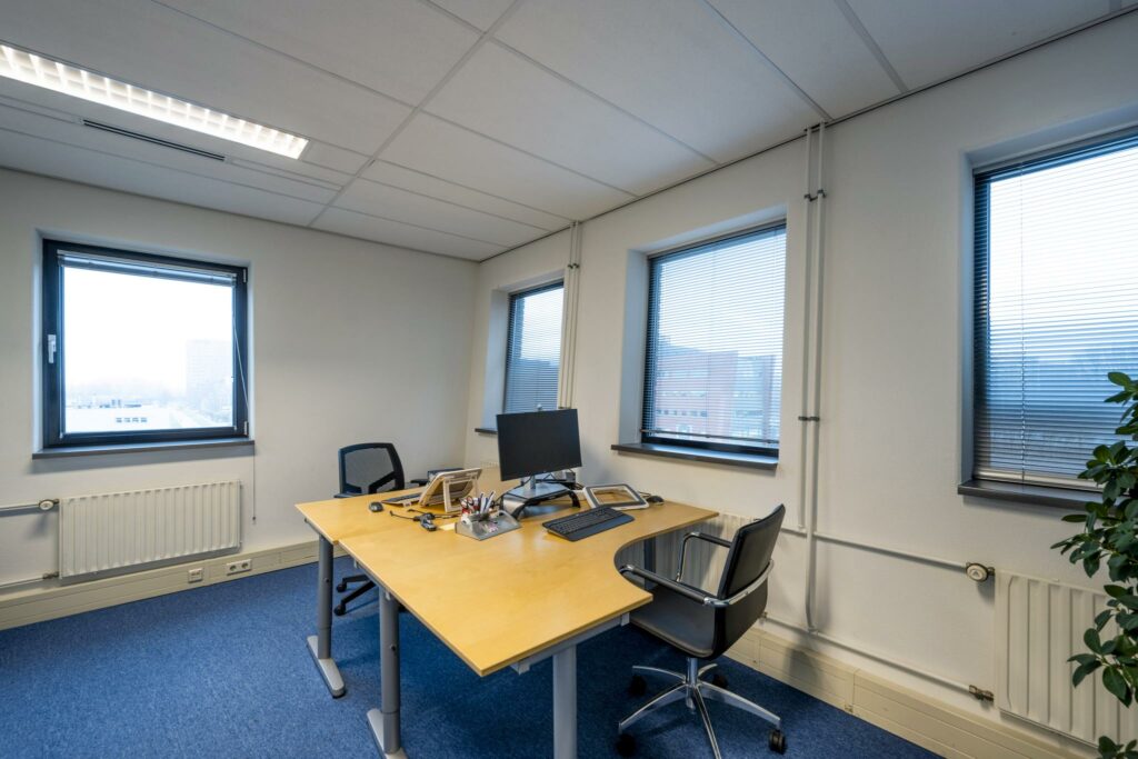 Modern ingericht kantoor aan de Joop Geesinkweg met twee bureaus, een computer en uitzicht op kantoorgebouwen.
